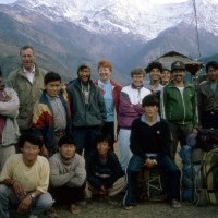 A group of trekkers posing in front of the Annapurna Base Camp sign, with the snow-capped Annapurna mountains in the background.